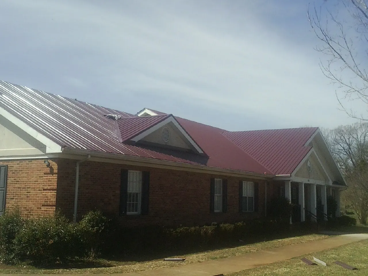 Red metal roof with gabled entries on a long brick building, from a Hail Damage Roof Repair job in Muncy