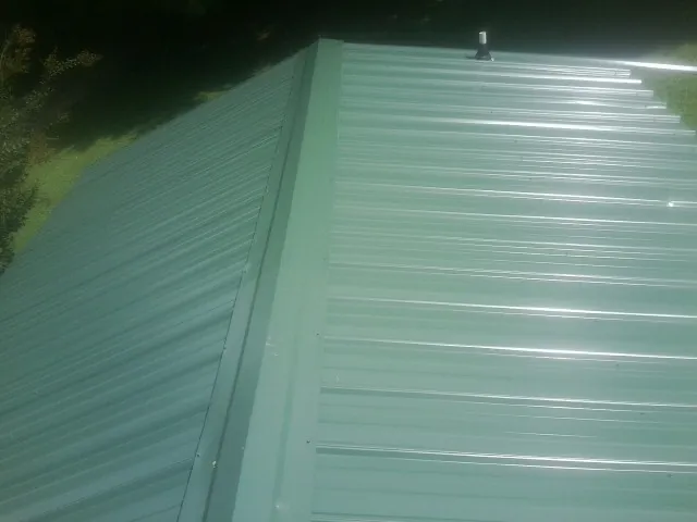 New green metal panels meeting at the ridge of a roof — Flat Roof Repair work by our crew in Muncy