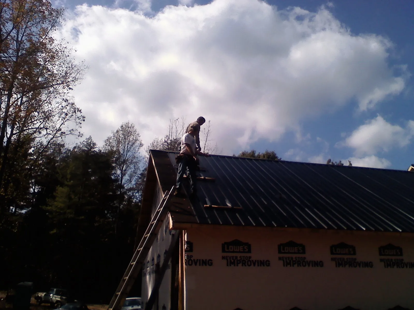 Roofer fastening dark metal panels high against a cloudy sky, from a Roof Inspection job in Muncy